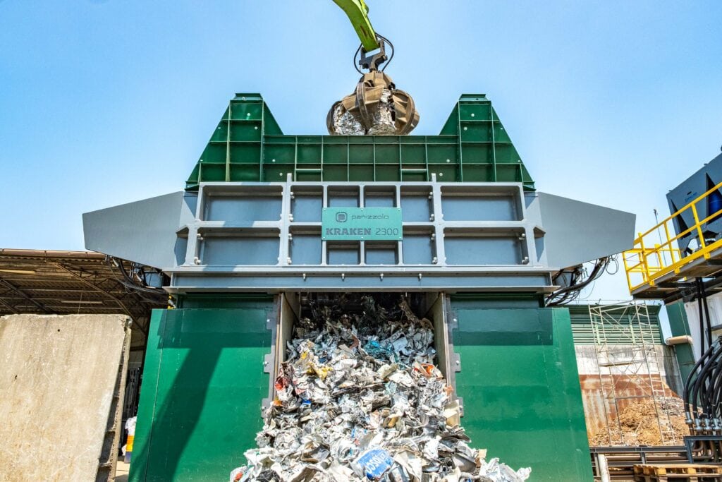 Industrial waste shredder processing recyclables at waste management facility.