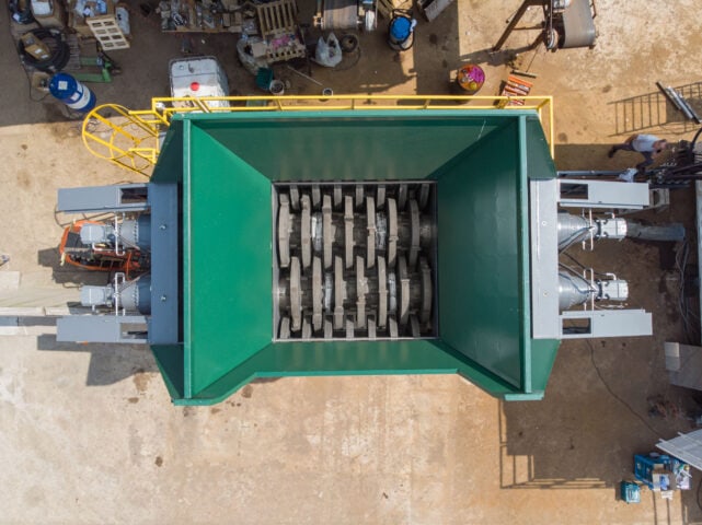Industrial waste pre-shredder with large rotating blades for recycling.